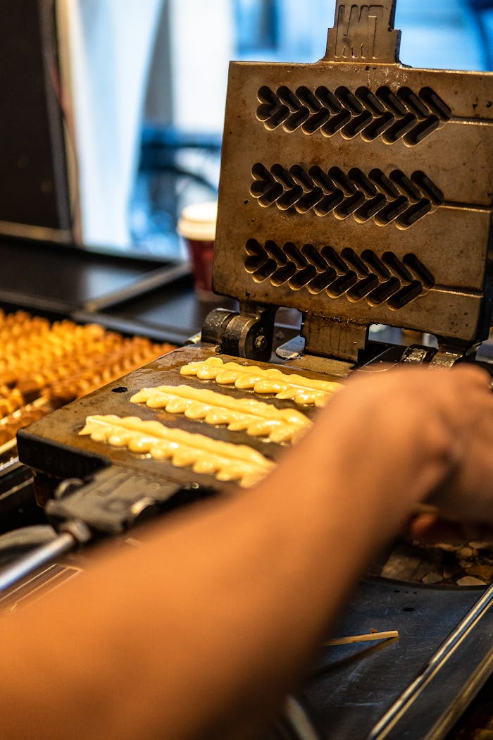 Close-up of traditional waffle maker in use, capturing the hand of a chef in Brugge, Belgium.